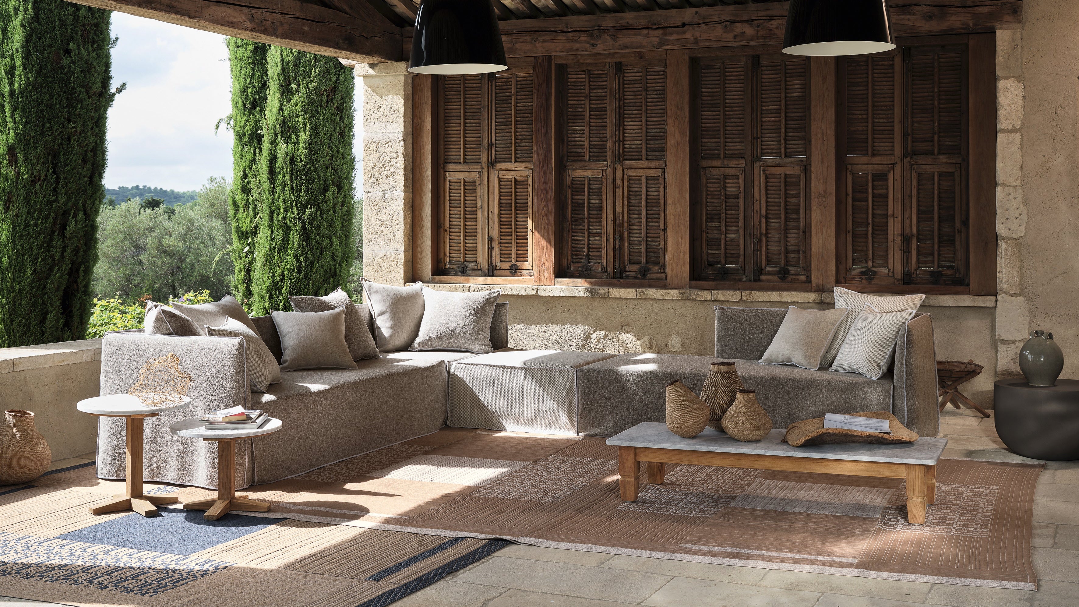 Outdoor patio with gray sectional sofa, wooden coffee table, and hanging lights under a rustic wooden roof.